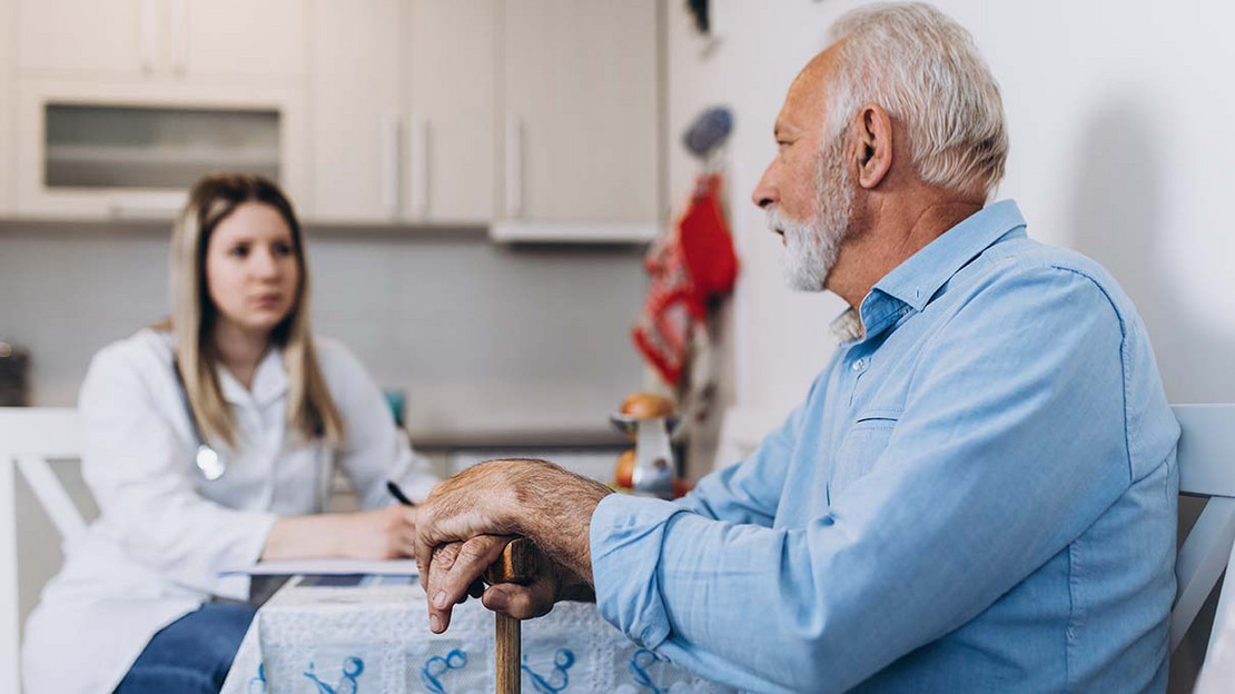 Eine Frau spricht mit ihrem älteren Vater an einem Küchentisch. 