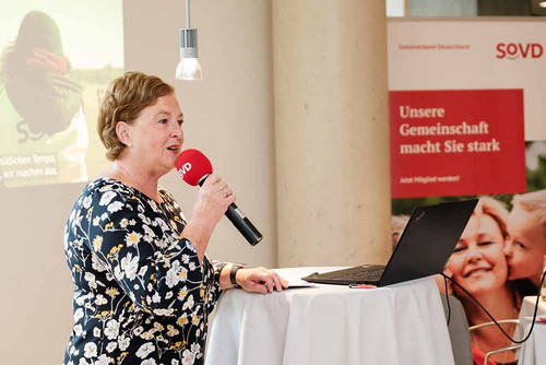 Frau steht an einem Pult und spricht in ein Mikrofon. 