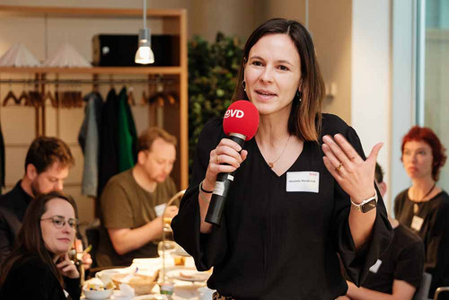 Frau redet in ein Mikrofon und unterstreicht das Gesagte gestisch mit den Händen. 