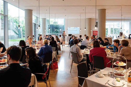 Vollbesetzter Saal, in dem Menschen an mehreren Tischen sitzen und frühstücken. 