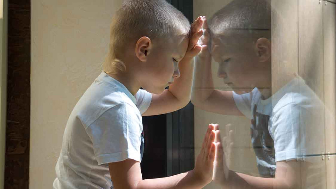 Einsames Kind blickt durch eine Fensterscheibe.