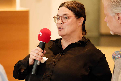 Frau sitzt in einem Rollstuhl und spricht in ein Mikrofon. 